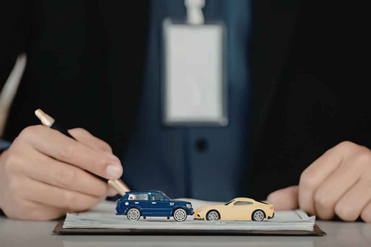 una mano con una penna dietro a due modellini di auto