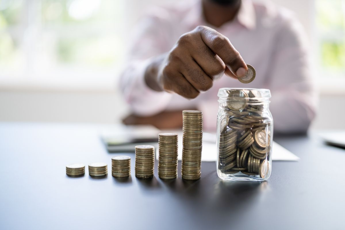 uomo che mette soldi di spiccioli in un barattolo di vetro