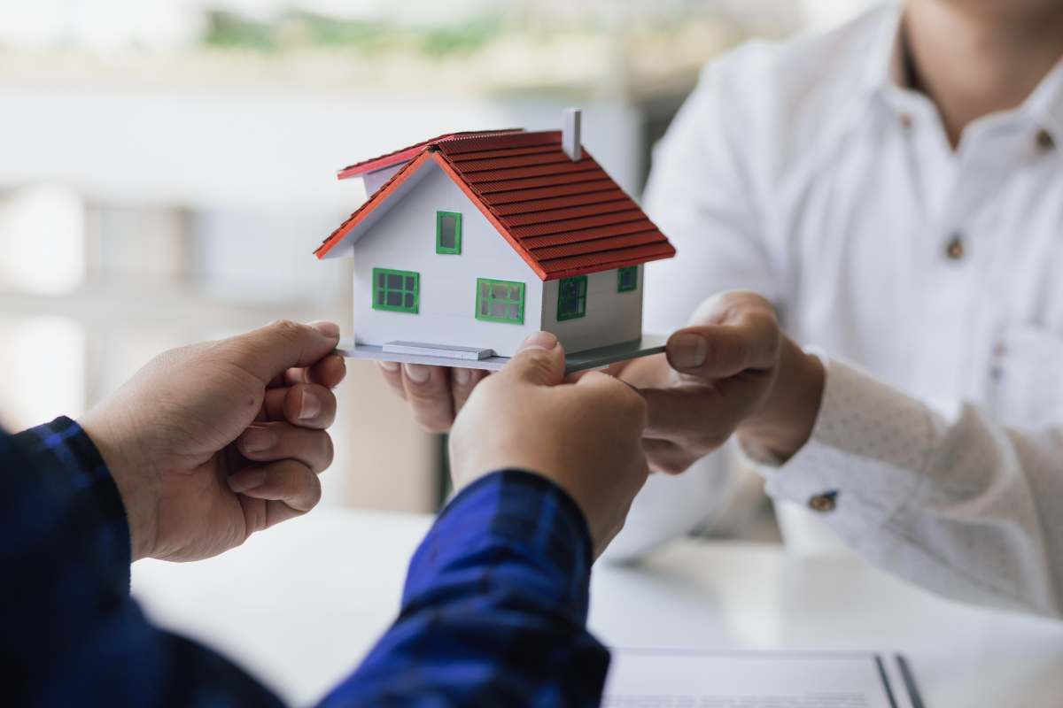 due persone che si passano il modellino di una casa 